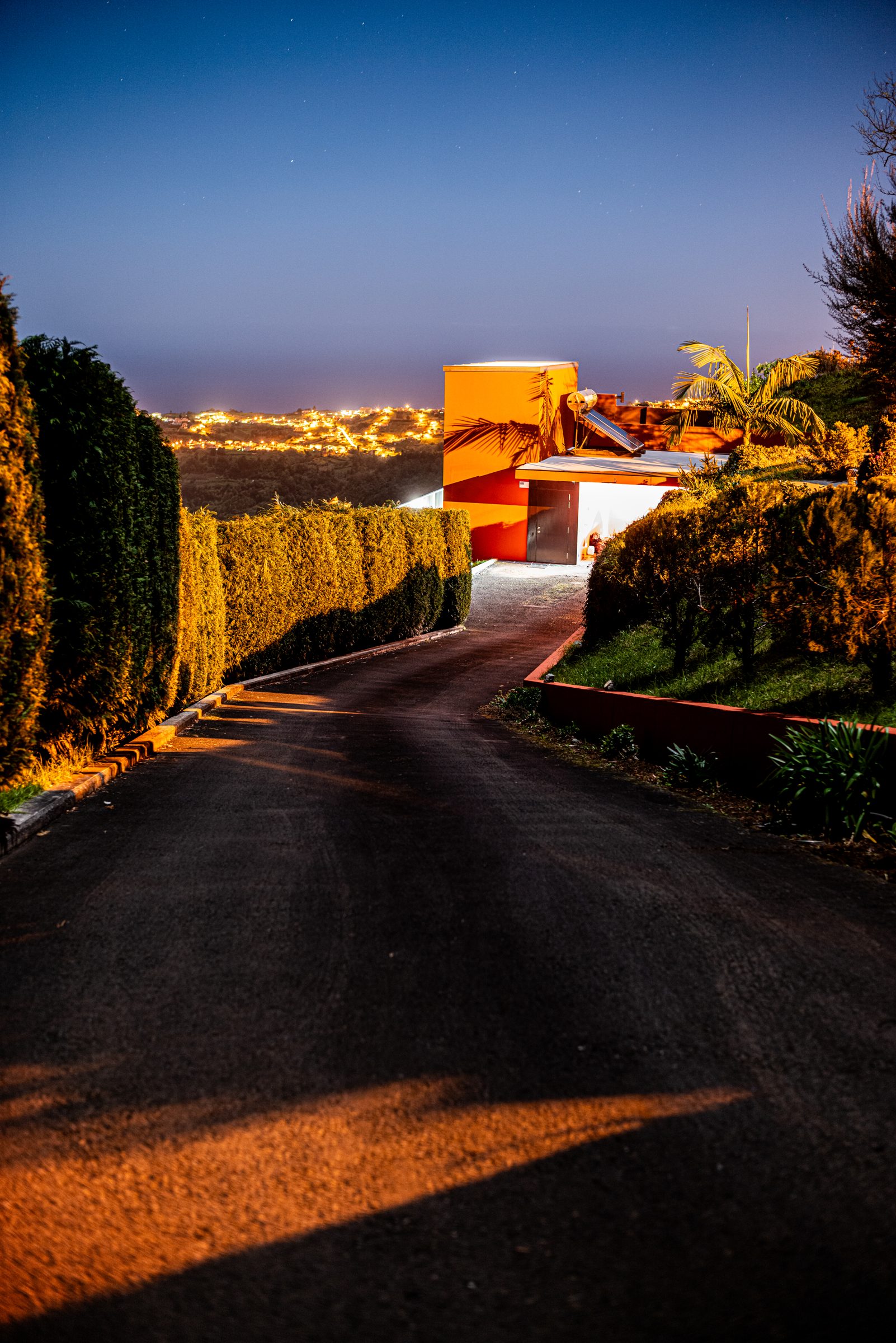 Night driveway leading to the orange villa, with town lights in the valley