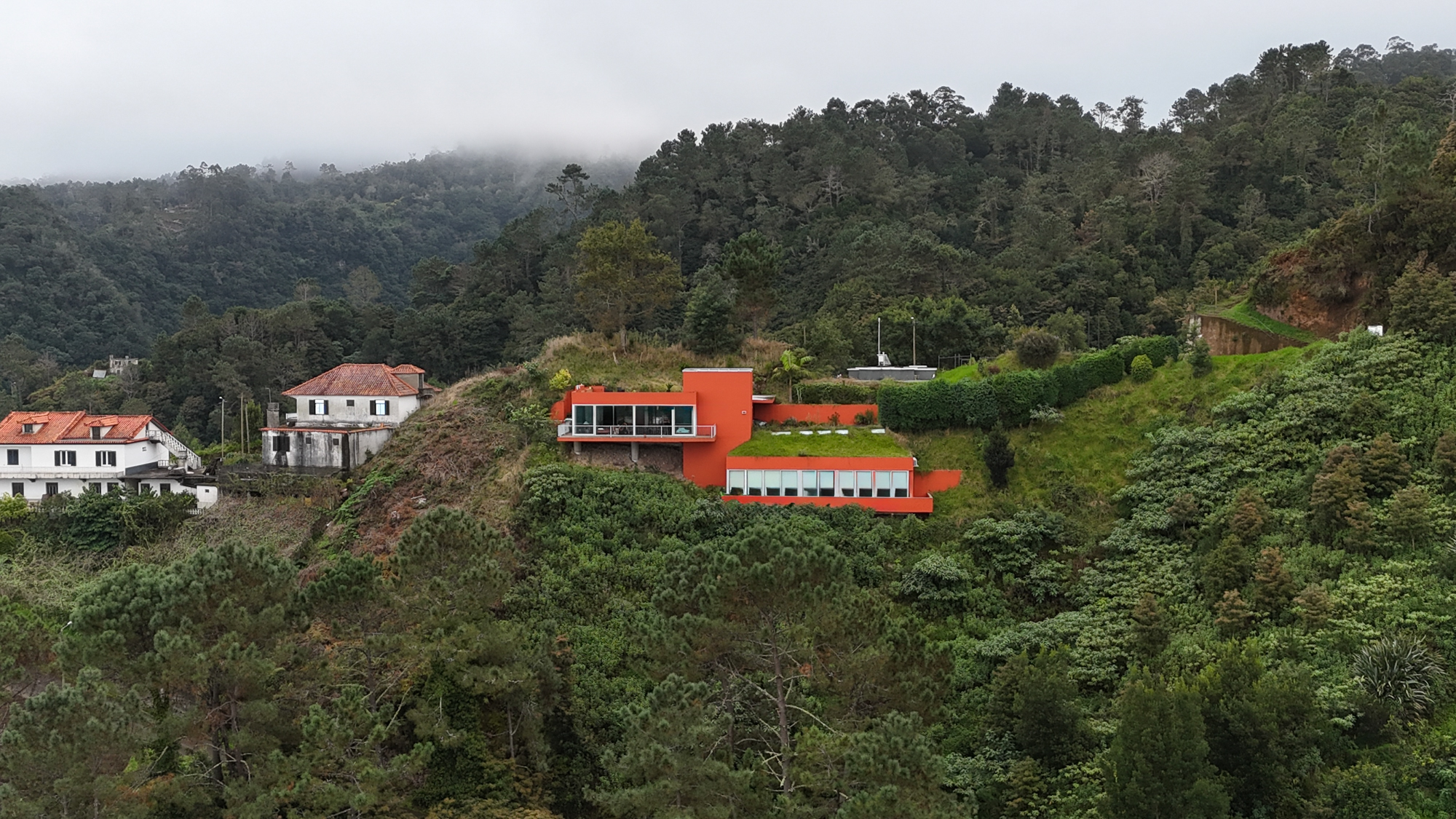 Orange villa on a misty Santana hillside, with a green roof and forested slopes