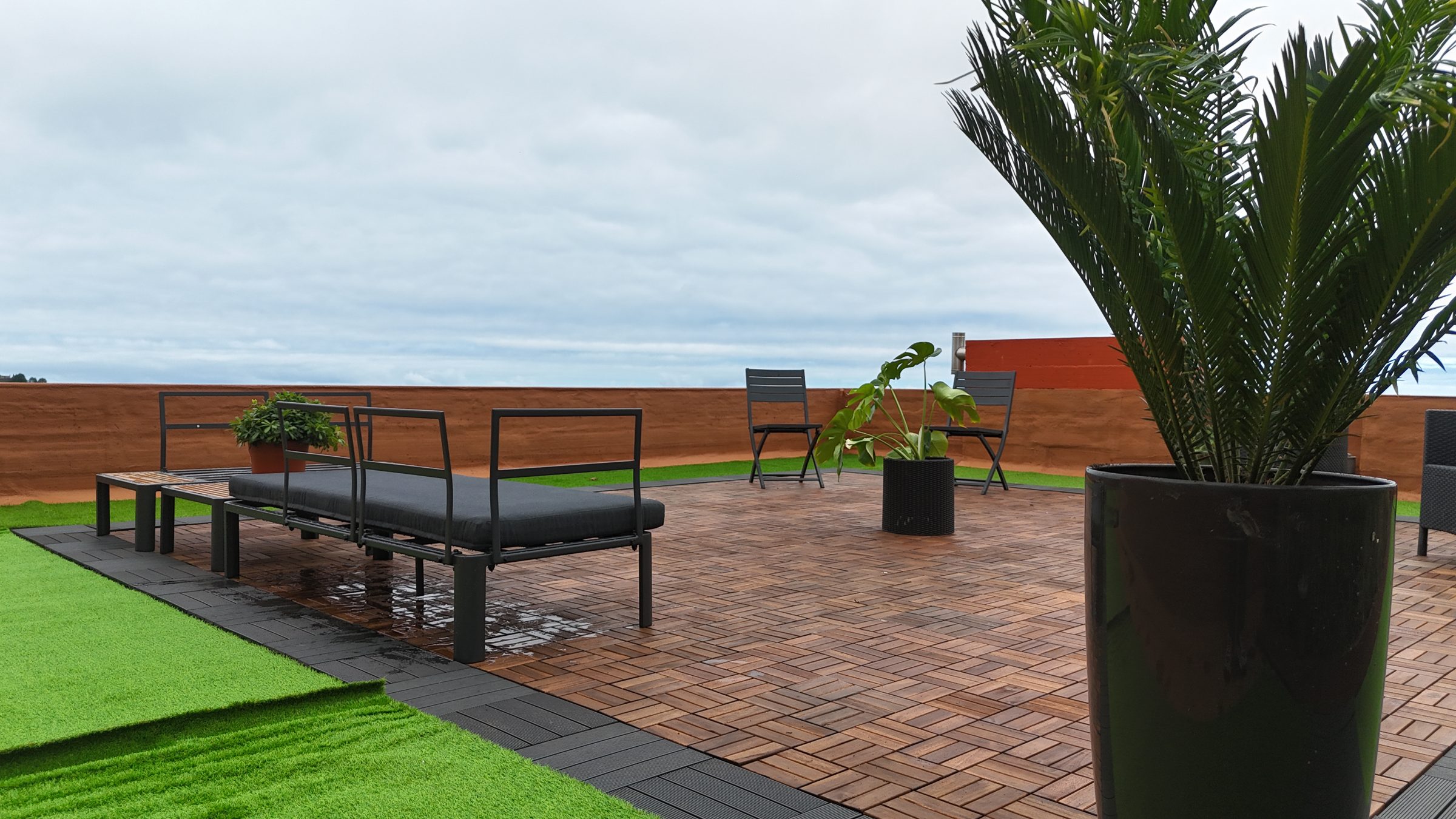 Rooftop terrace with black lounge furniture, wood decking, a potted palm, and the horizon beyond