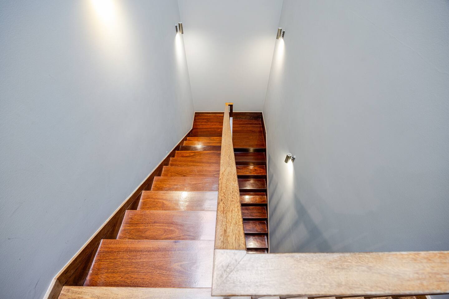 Looking down the dark wood staircase with a central rail and warm wall lights