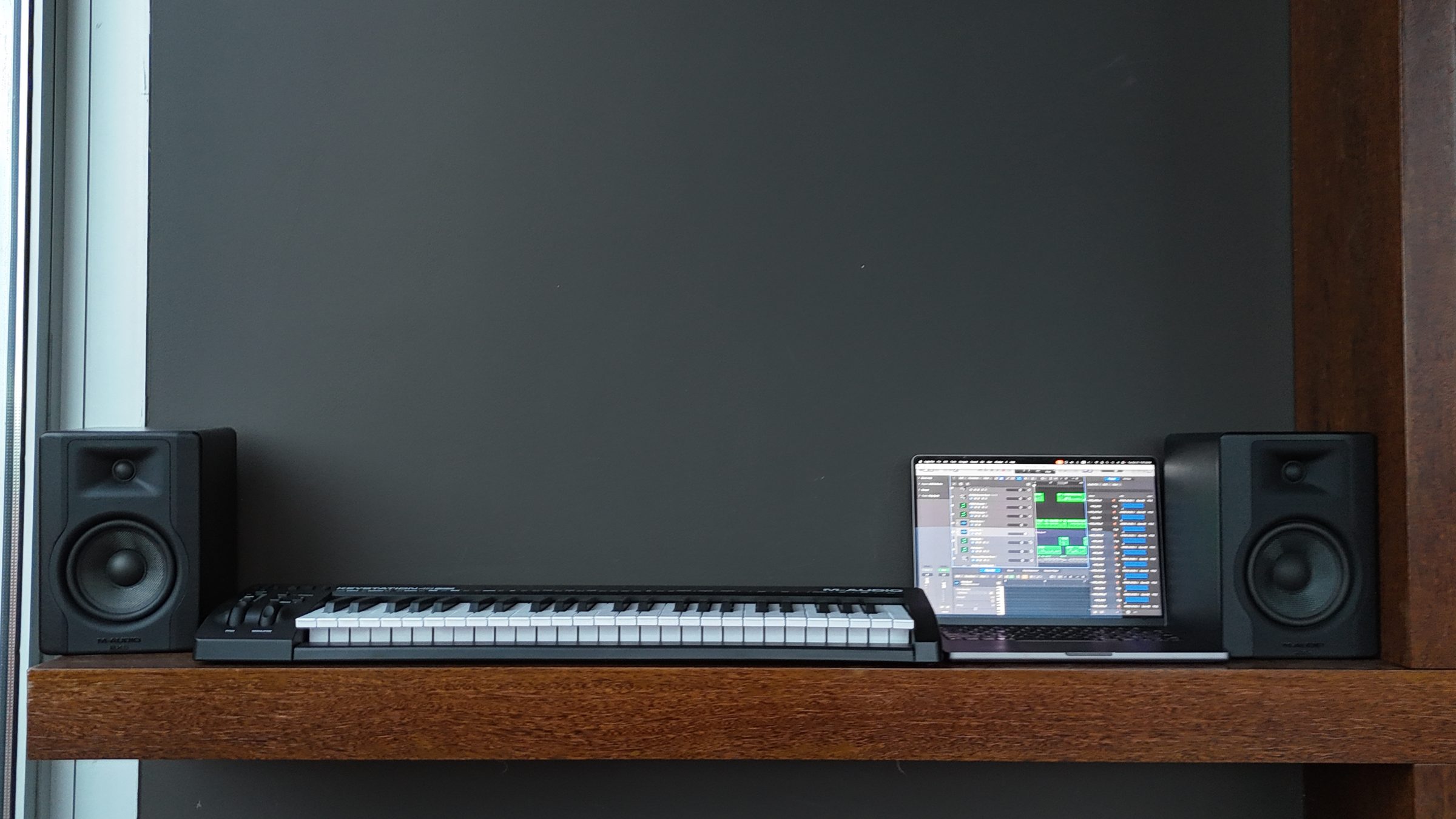Music studio with a MIDI keyboard, monitors, and laptop on a wood shelf
