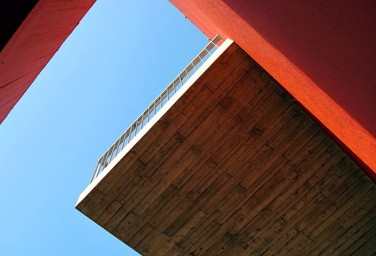 Looking up between orange walls at a cantilevered balcony and blue sky