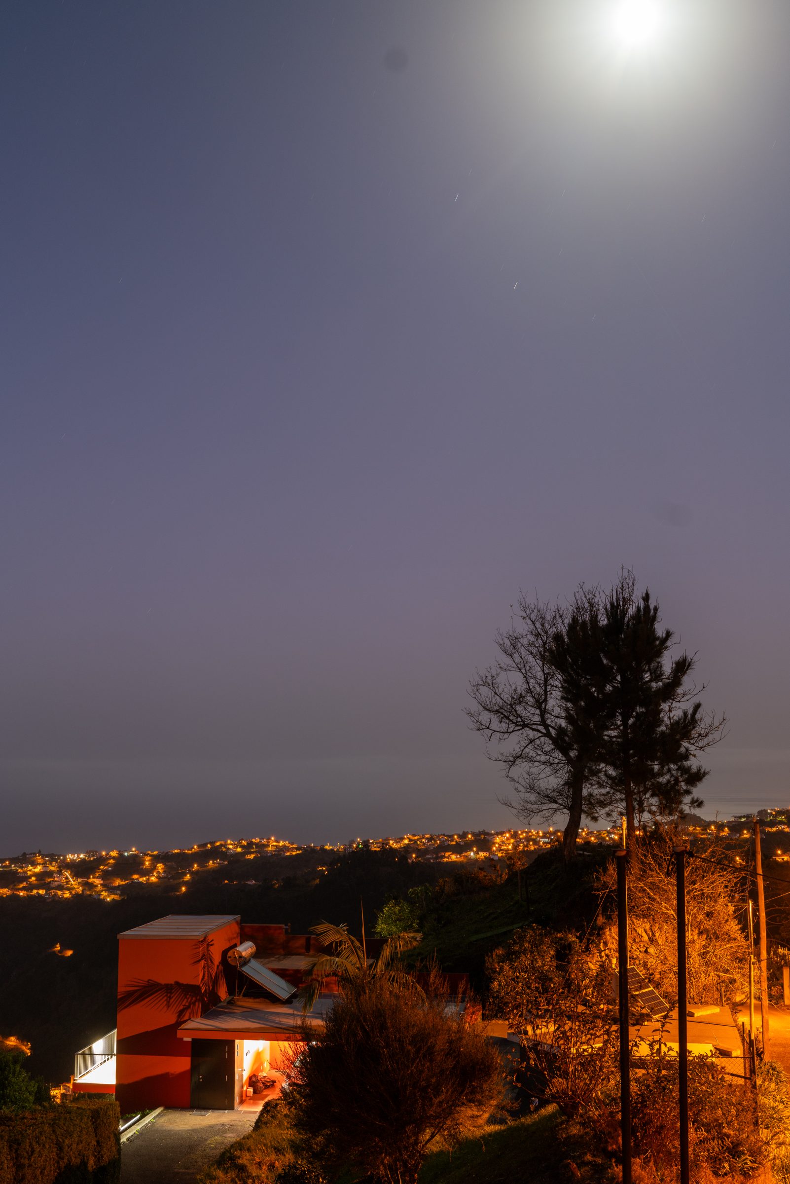 Night view of the orange villa under a bright moon, with Santana lights below