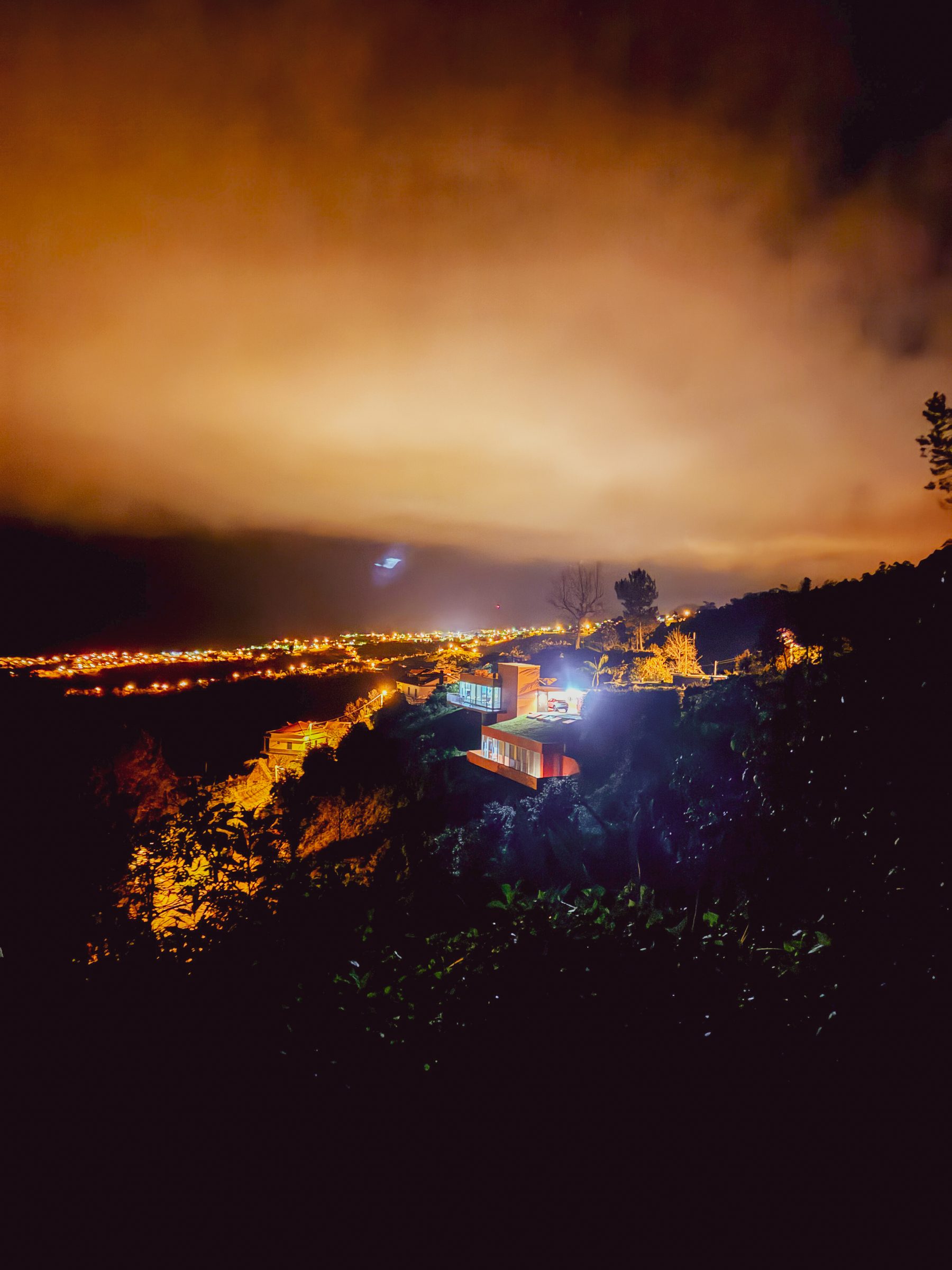 Casa Keam at night on the hillside, with valley lights under an amber sky