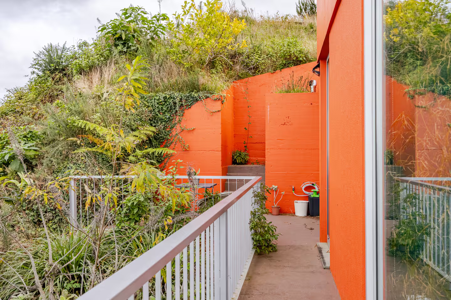 Orange exterior walkway with a white railing and hillside plants