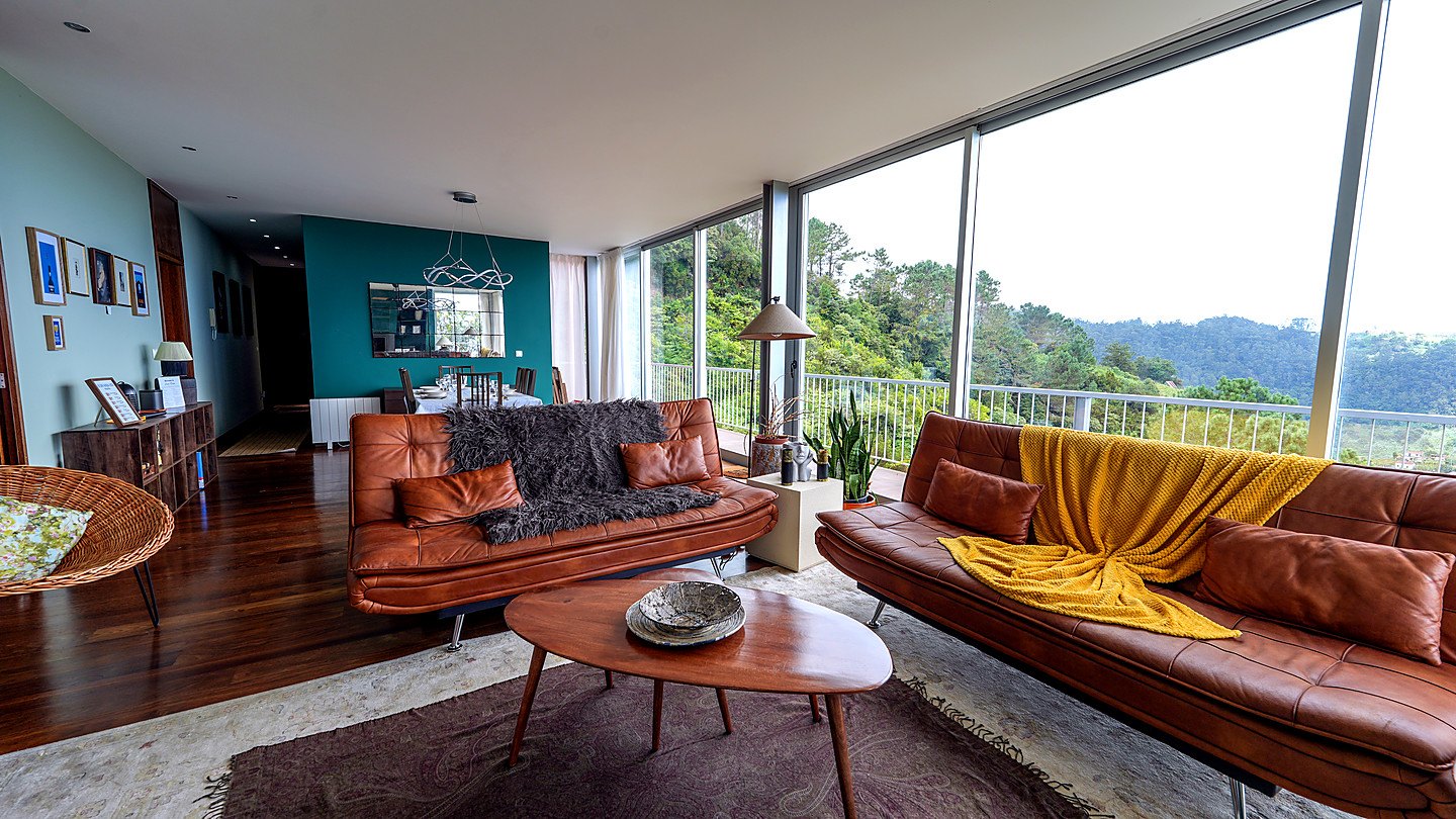 The living room: two leather sofas, a wall of glass and the forest beyond the terrace rail