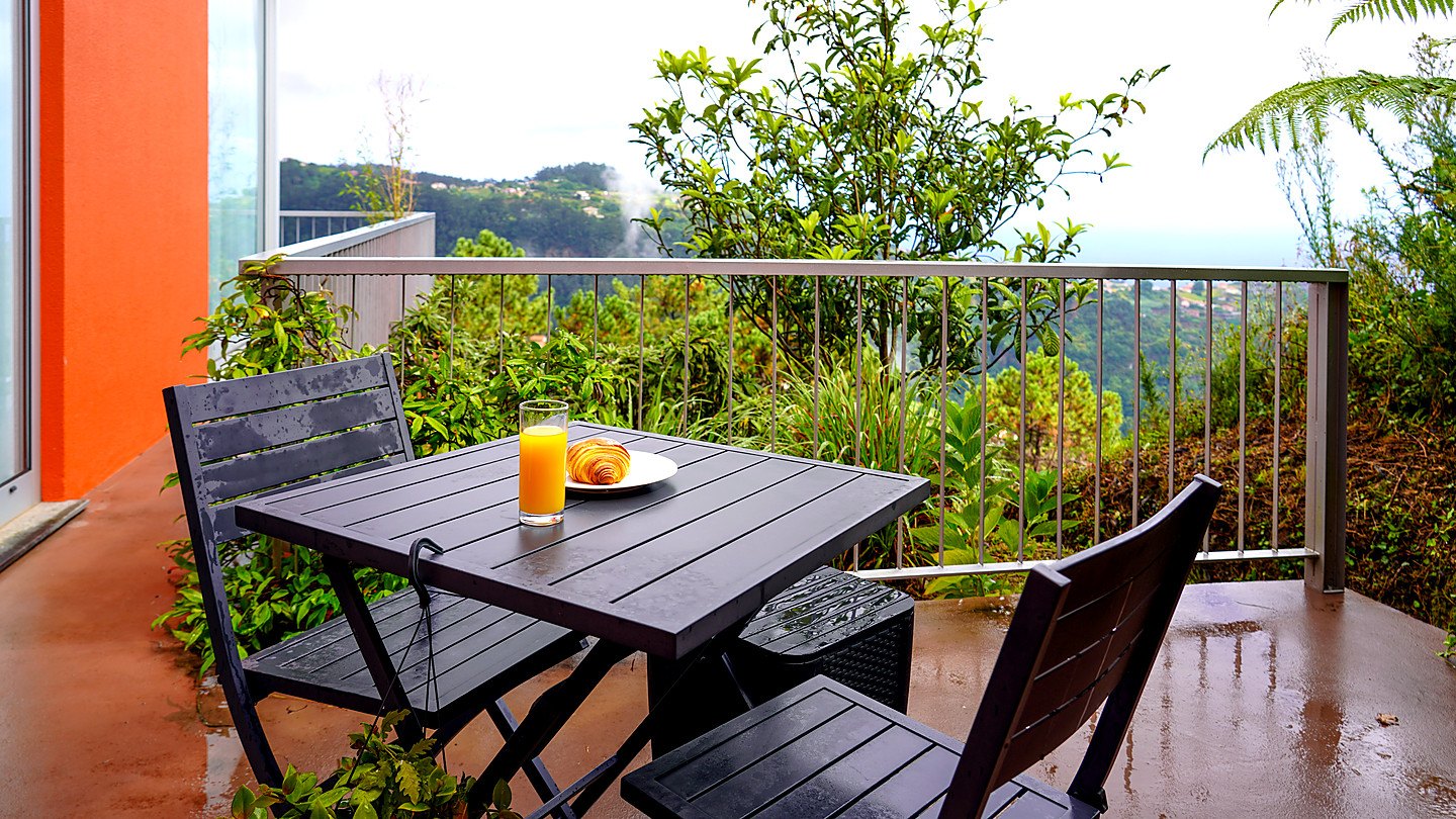Breakfast on the terrace: orange juice and a croissant on a table by the rail, the forested valley beyond