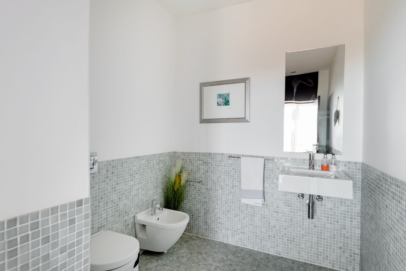 Bagno di servizio con mosaico, lavabo a parete e specchio