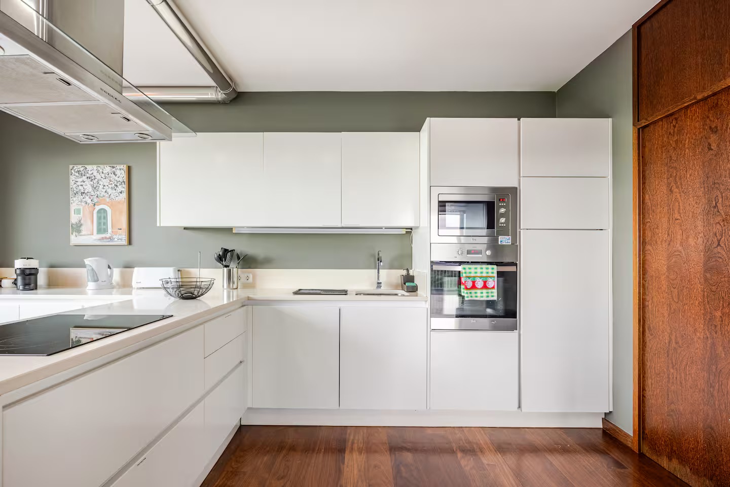 Kitchen with white cabinets, induction cooktop, steel hood, and built-in oven