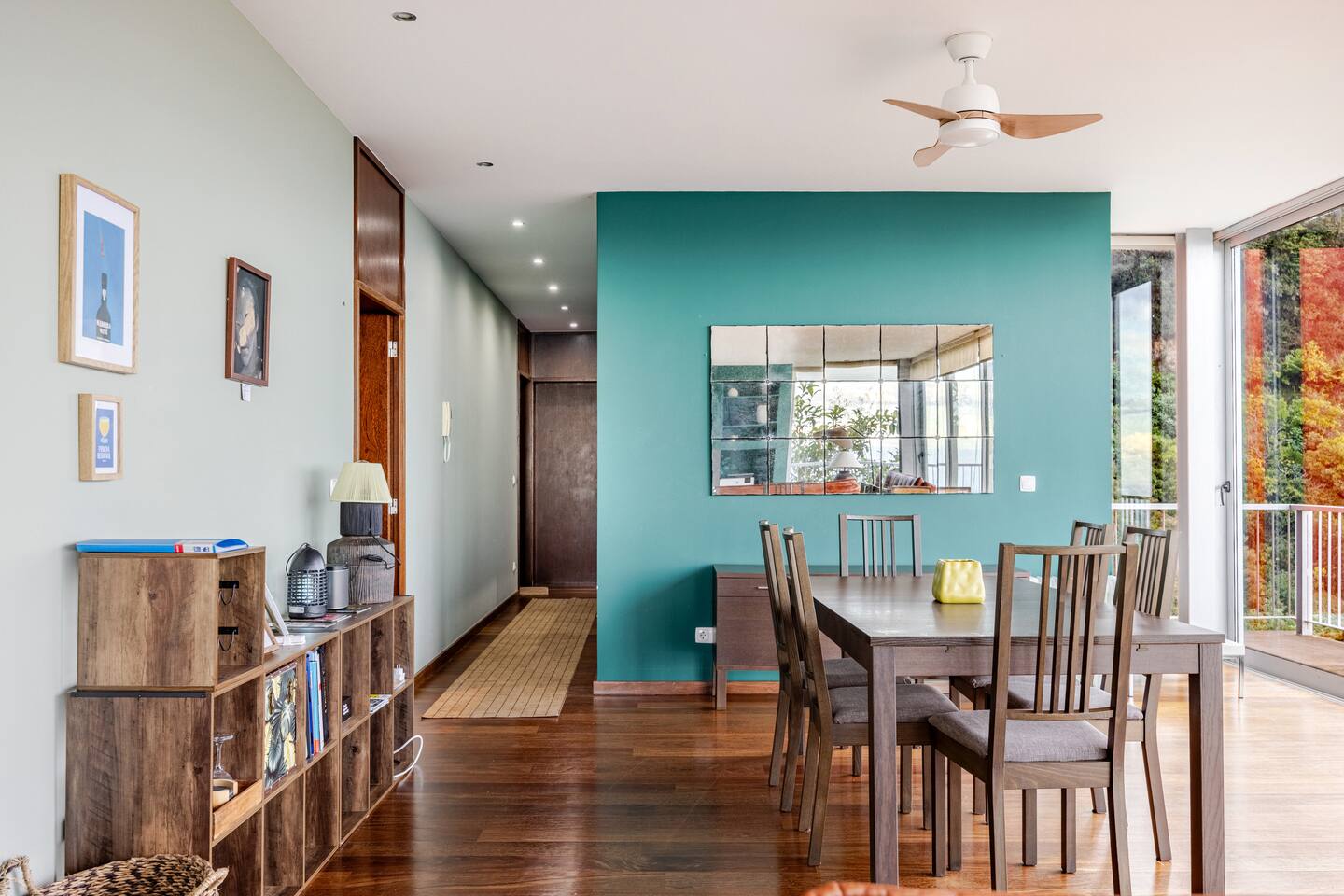 Dining table against a teal wall with a paneled mirror and the hallway beyond
