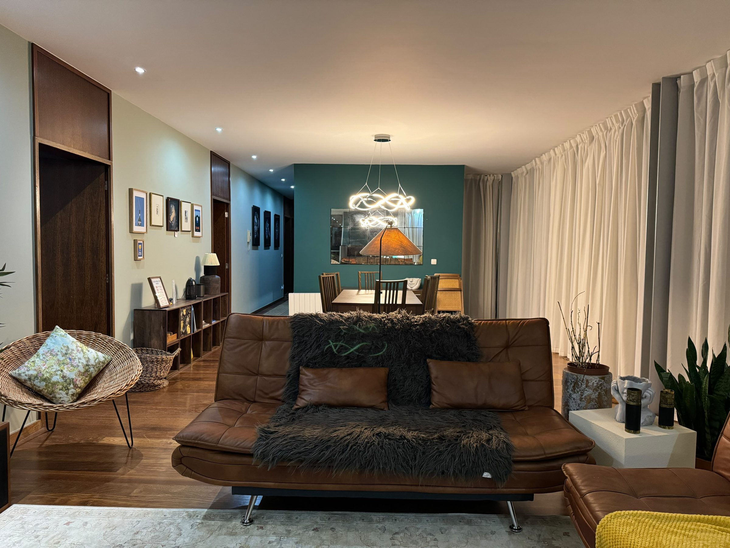 Living room with a leather sofa, wicker chair, and dining table against a teal wall