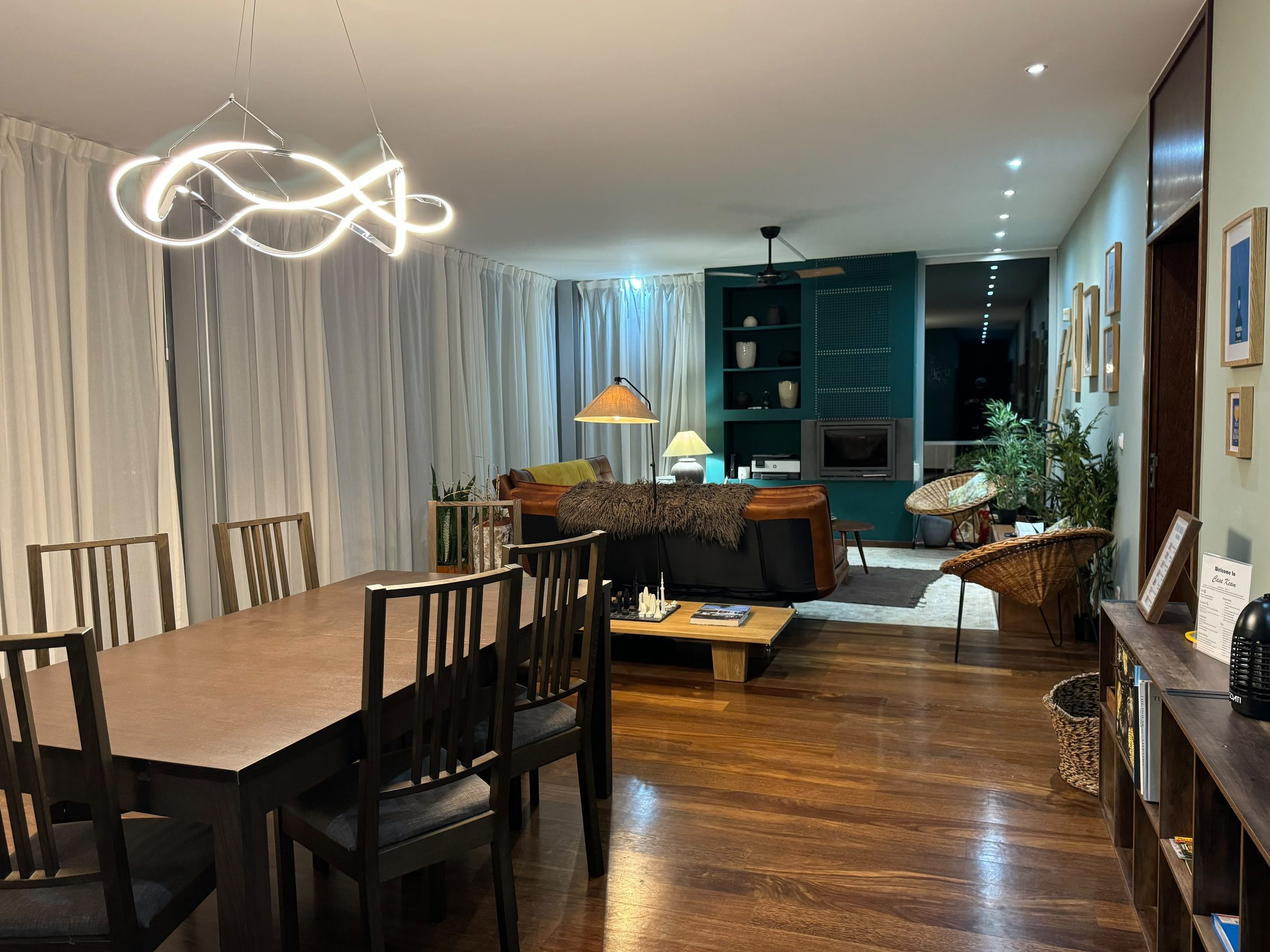 Open living and dining room with a wavy chandelier, leather sofa, and teal fireplace wall