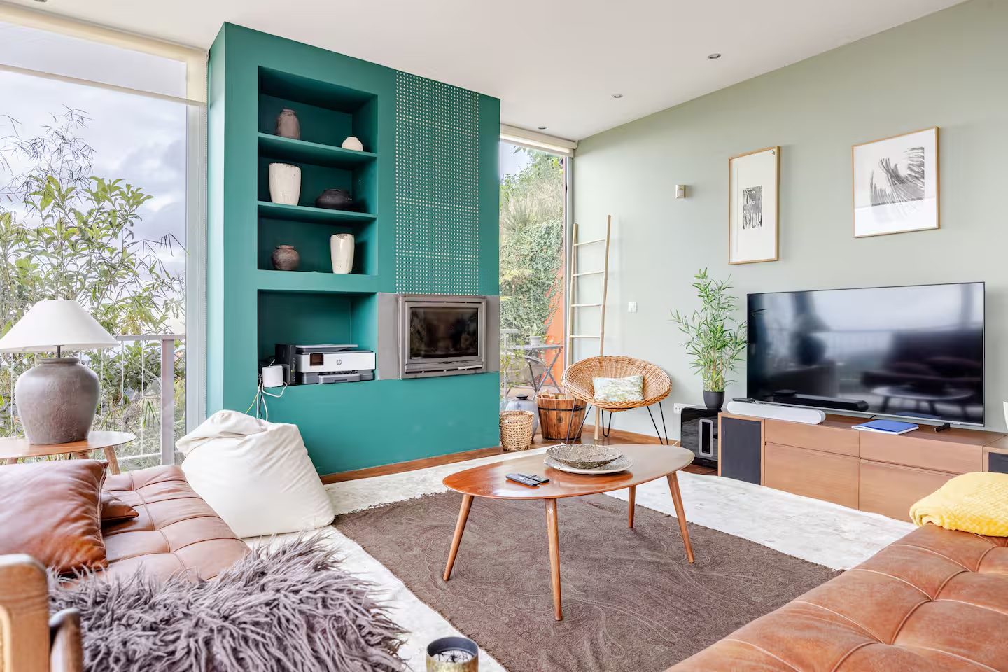 Wohnzimmer mit petrolfarbener Kaminwand, Ledersofas und Blick in den Garten