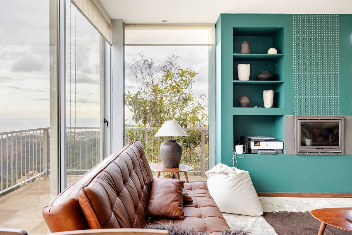 living room with a brown leather sofa, teal fireplace wall, and balcony looking to the hills