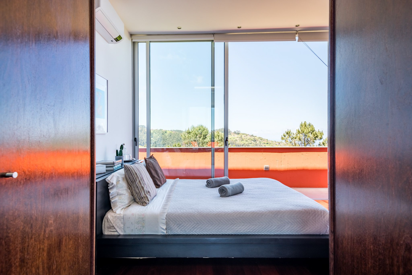 Master bedroom seen through the doorway, with the orange terrace and hills beyond