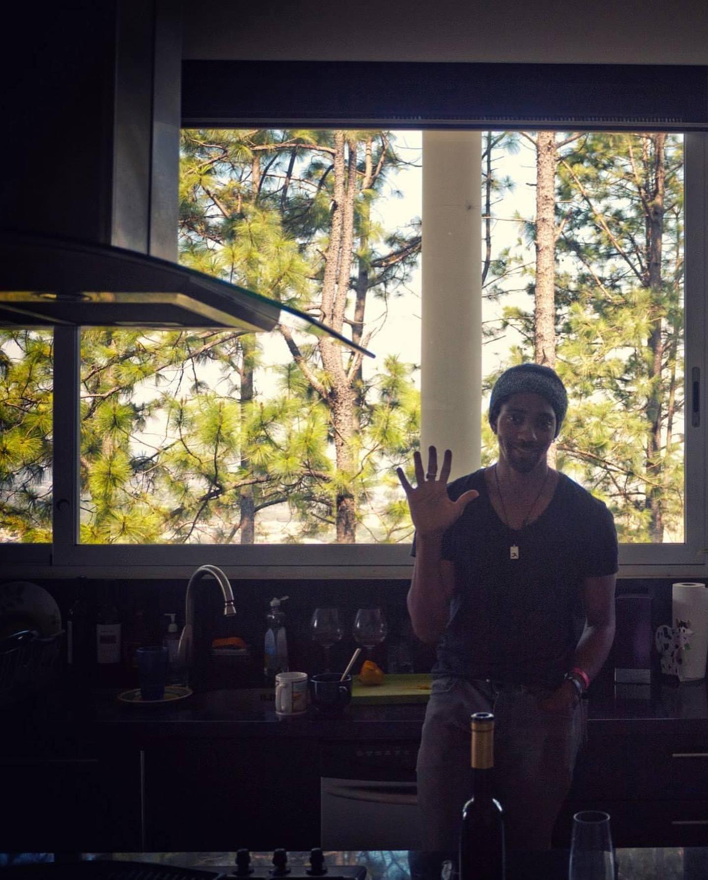 Keem waving from the kitchen, forest in the window behind him