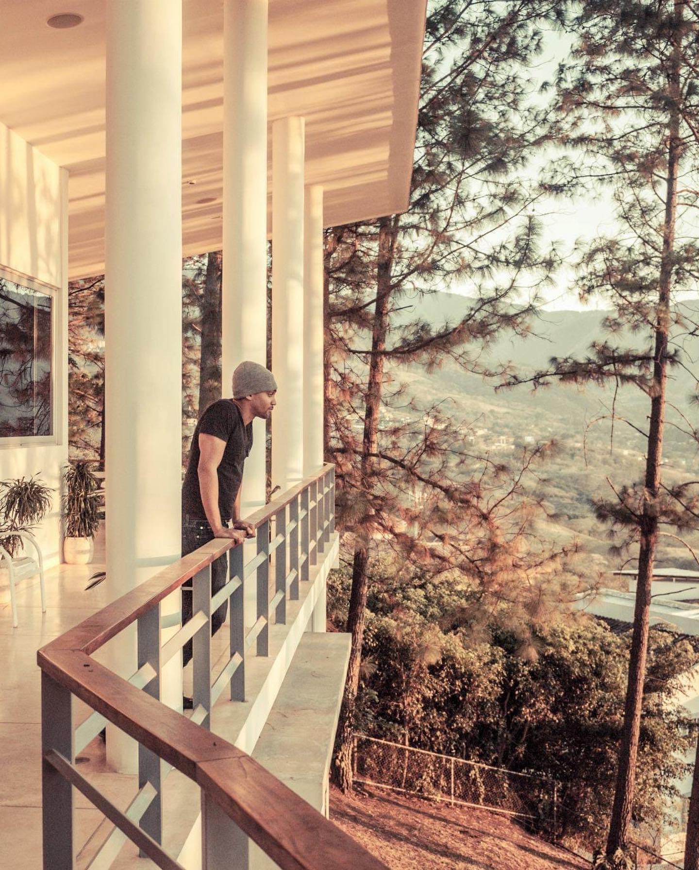 Keem on a columned balcony looking out over pine trees and a valley