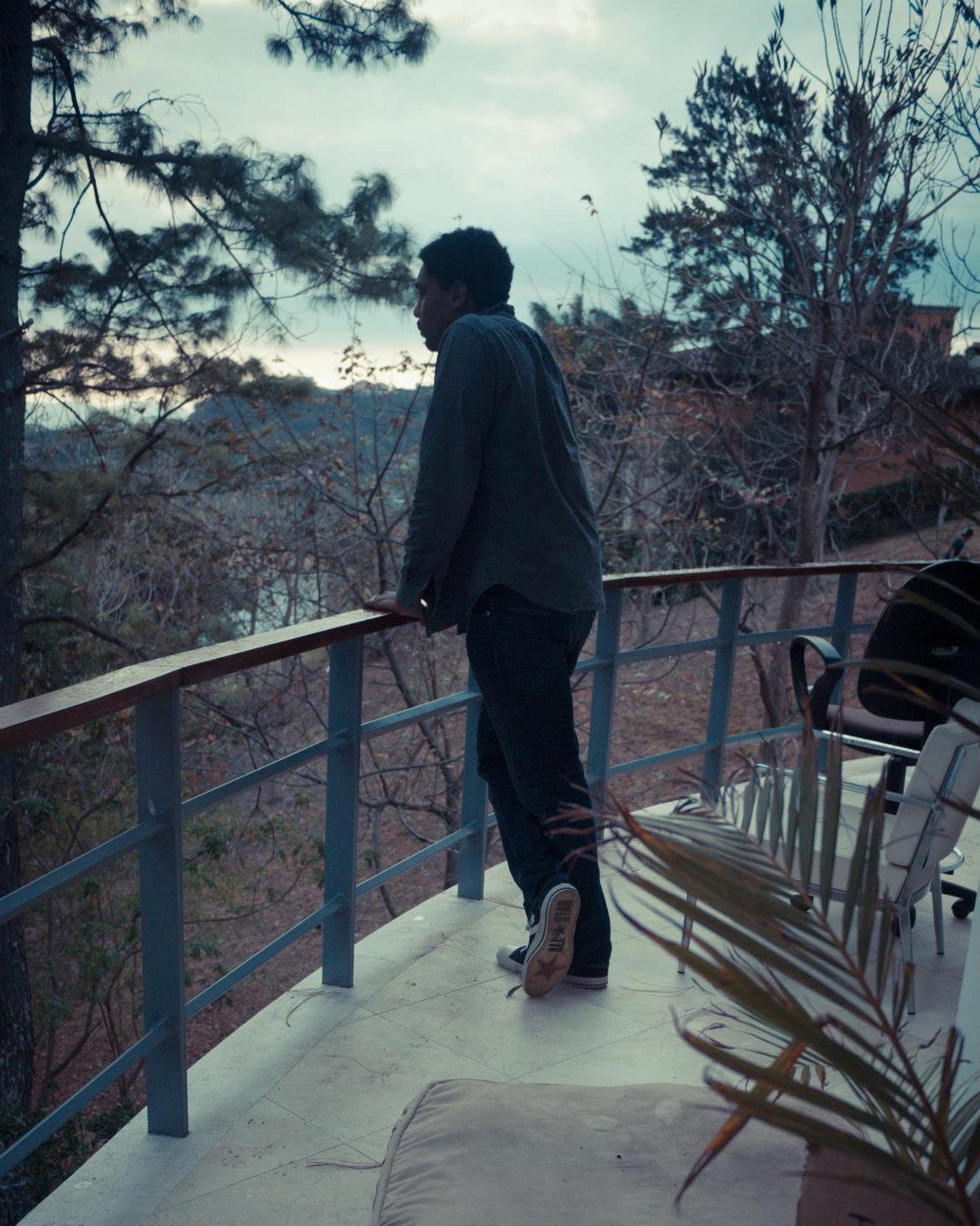 Keem on a terrace at dusk, looking out through the trees